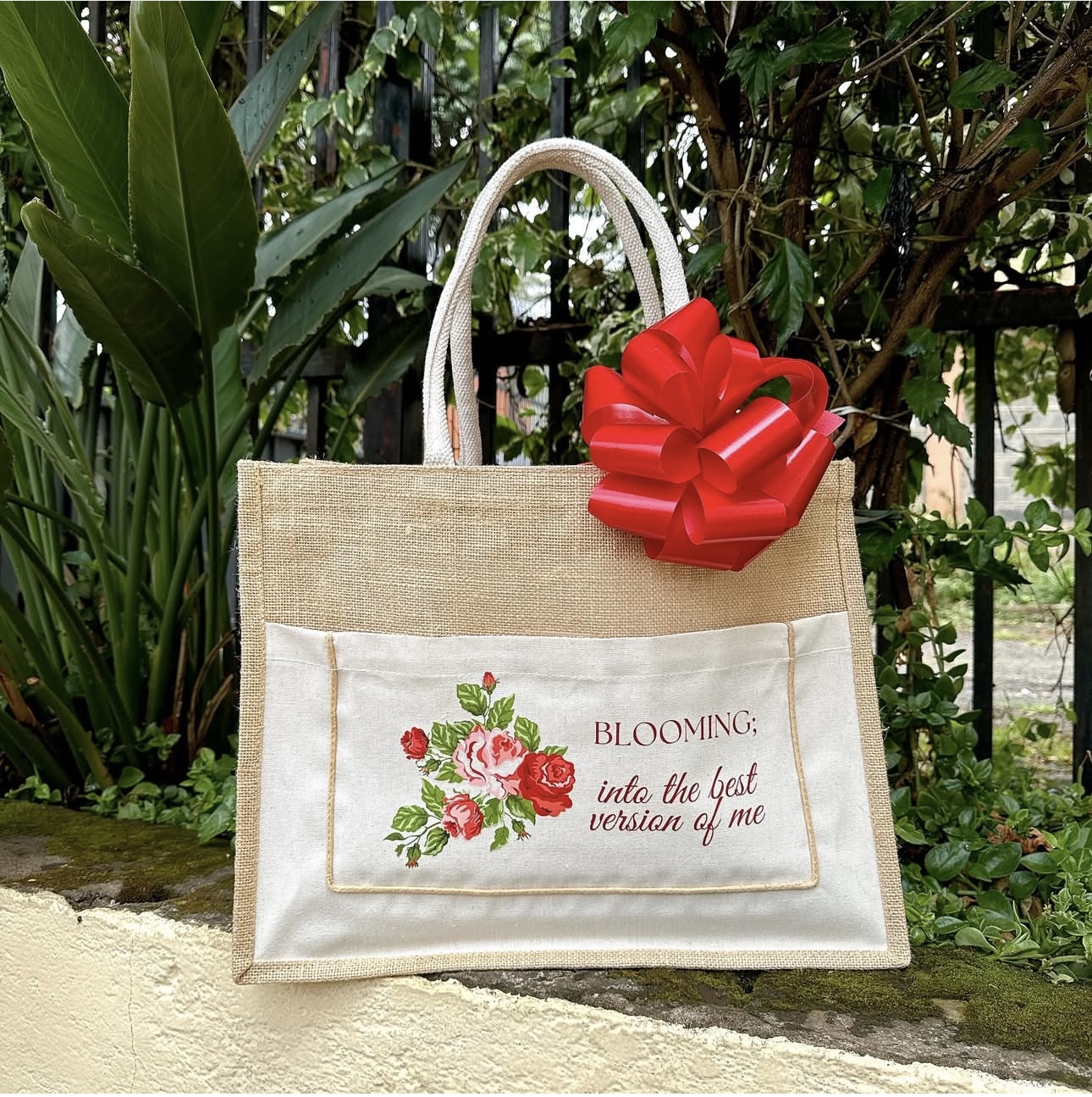 Floral print jute tote bag with 'Blooming into the best version of me' design and red gift bow by Gifting Kenya.